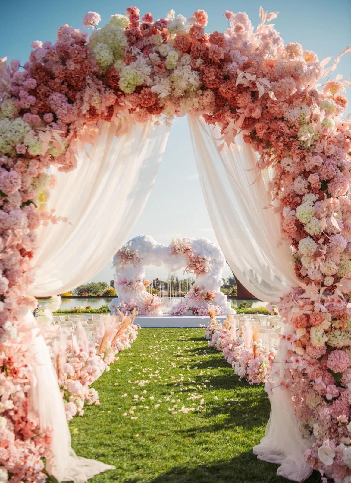 Un arco di rose rosa e tende bianche incornicia la navata e, in fondo, l'altare a forma di nuvola davanti al laghetto