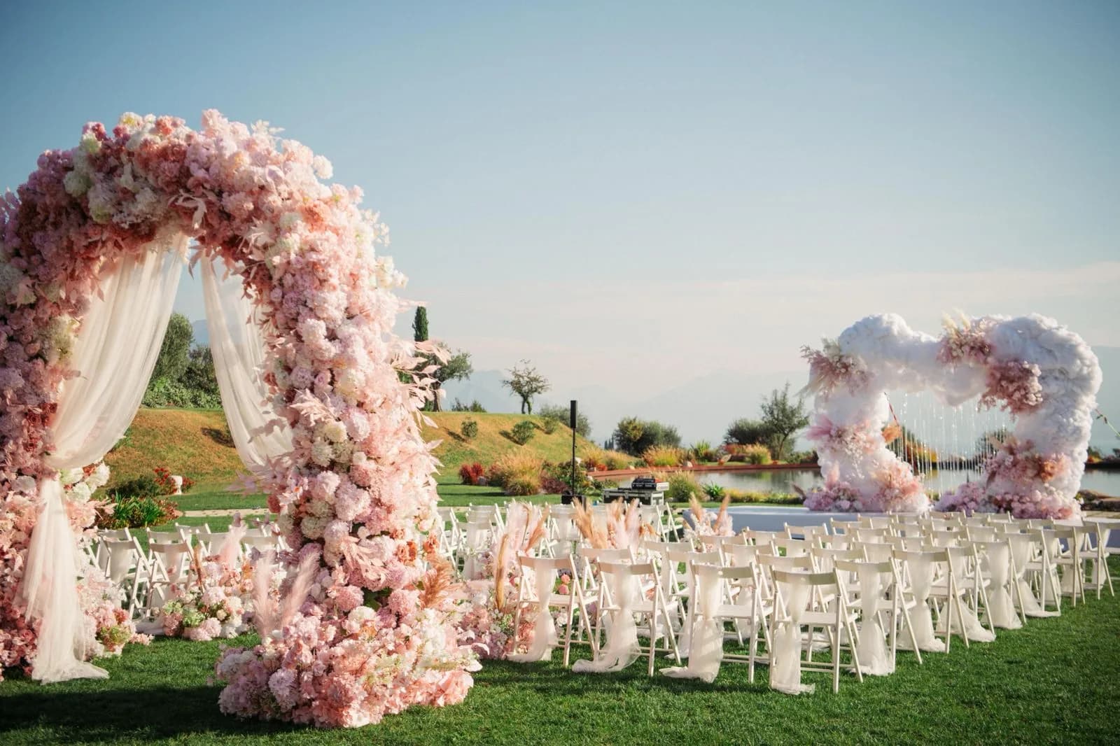 Un arco di fiori rosa sul prato e, oltre le sedie, l'altare a nuvola contro il cielo
