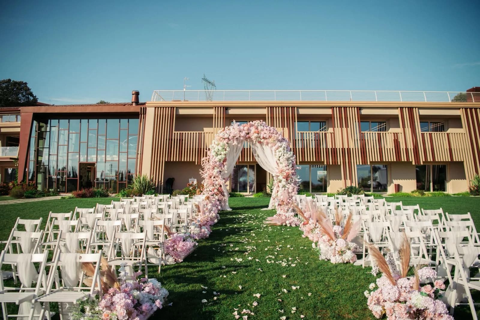 La navata sul prato, fra file di sedie bianche, porta a un arco di fiori davanti alla facciata della cantina