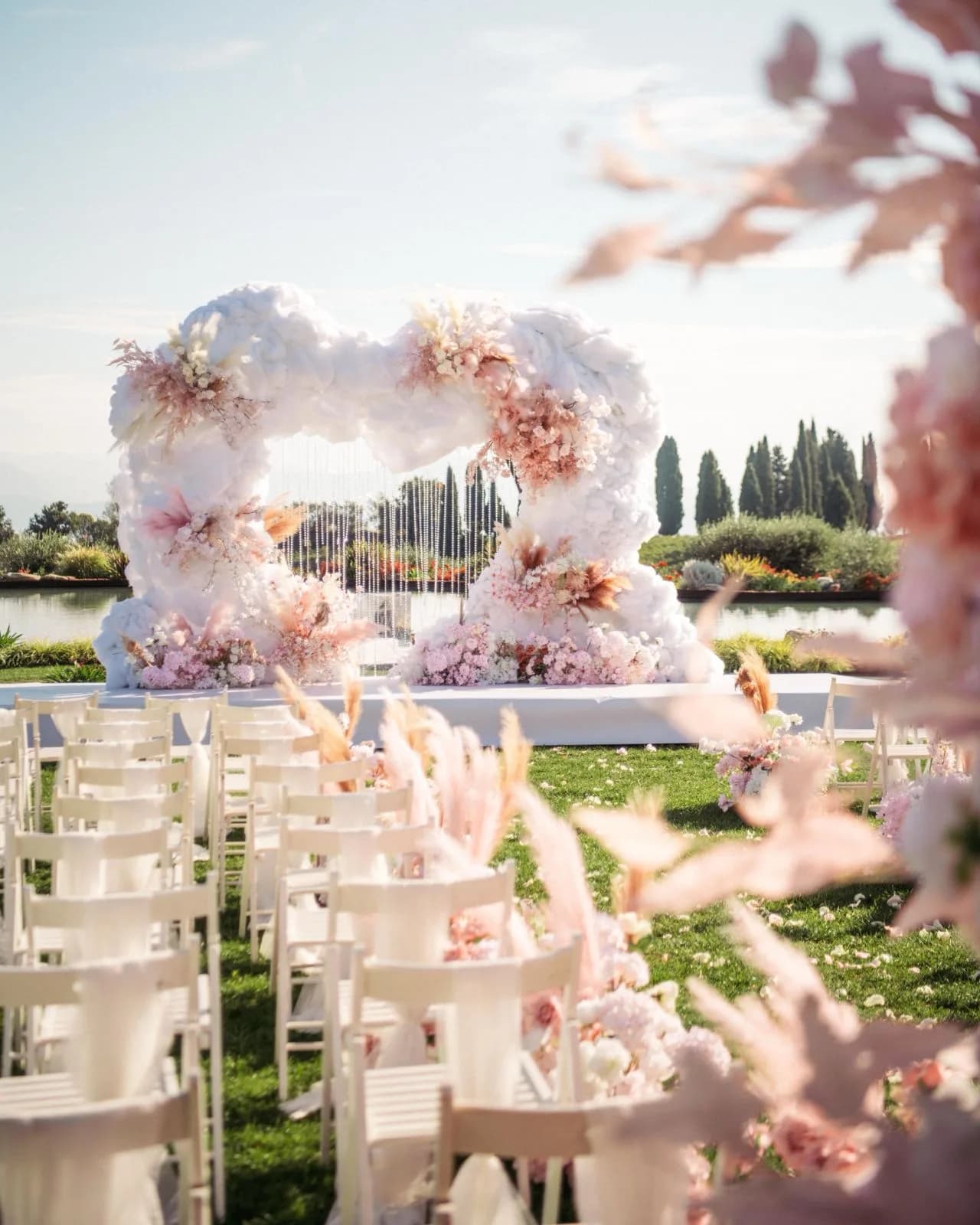 File di sedie bianche decorate di fiori davanti all'altare a nuvola, con i cipressi sullo sfondo